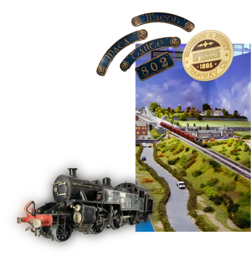 Model train display with a black steam locomotive and miniature landscape. Overhead are blue signs with gold text reading “Black Hawke” and a gold coin with “Beaconsfield Tramway 1885.”.