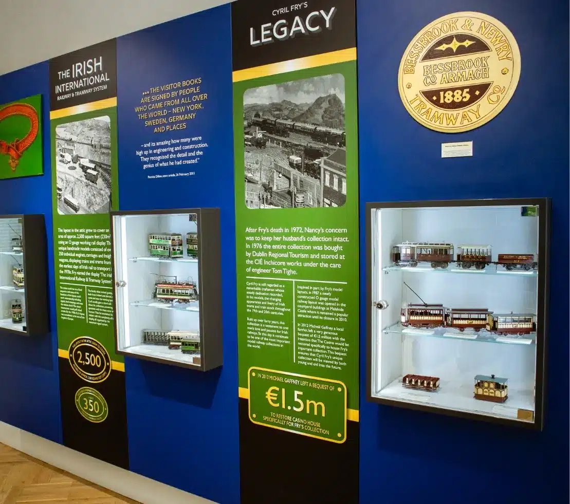 Exhibit display featuring model trains and historical information about Irish railways. Green and blue panels showcase text, images, and memorabilia, including a plaque dated 1885 and a sign noting a collection value of €1.5m.