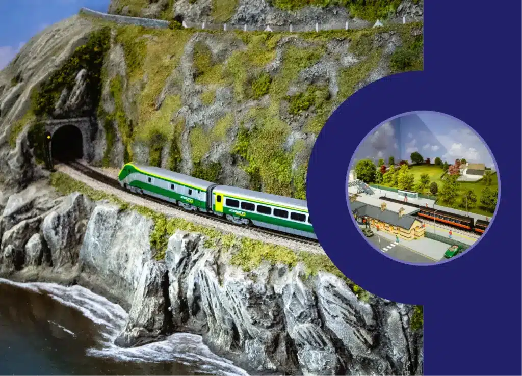 A model train travels through a tunnel in a rocky, mountainous landscape beside water. An inset circle reveals a miniature village with a station and houses amid trees, reminiscent of the charm surrounding Malahide Castle, all set against a serene blue backdrop.