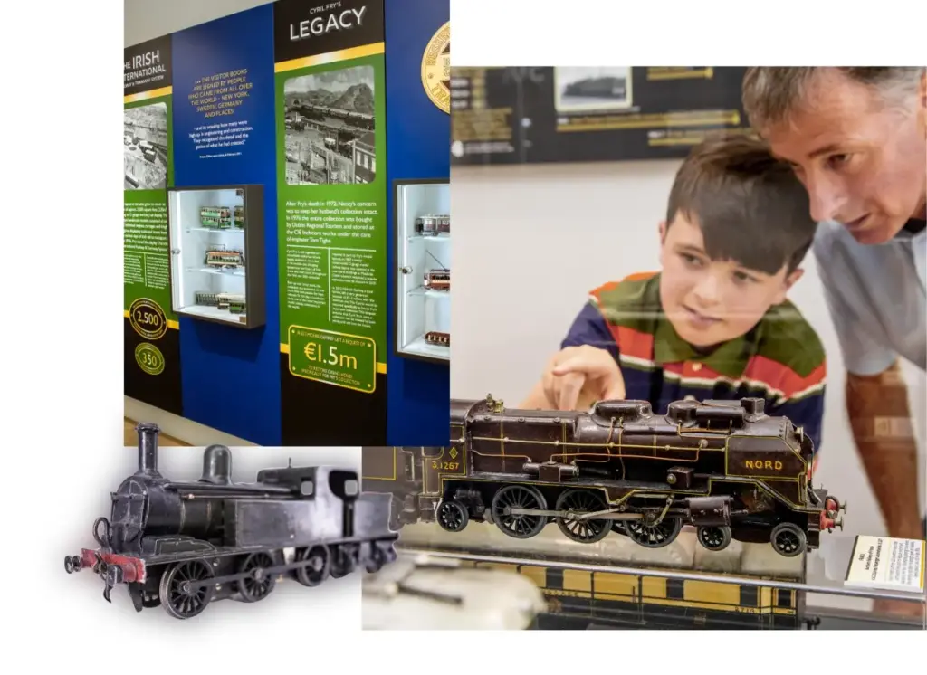A boy and an older man look at model trains. To the left, a museum exhibit displays information panels and cases with historic Irish railway artifacts. Two model trains are shown at the bottom.