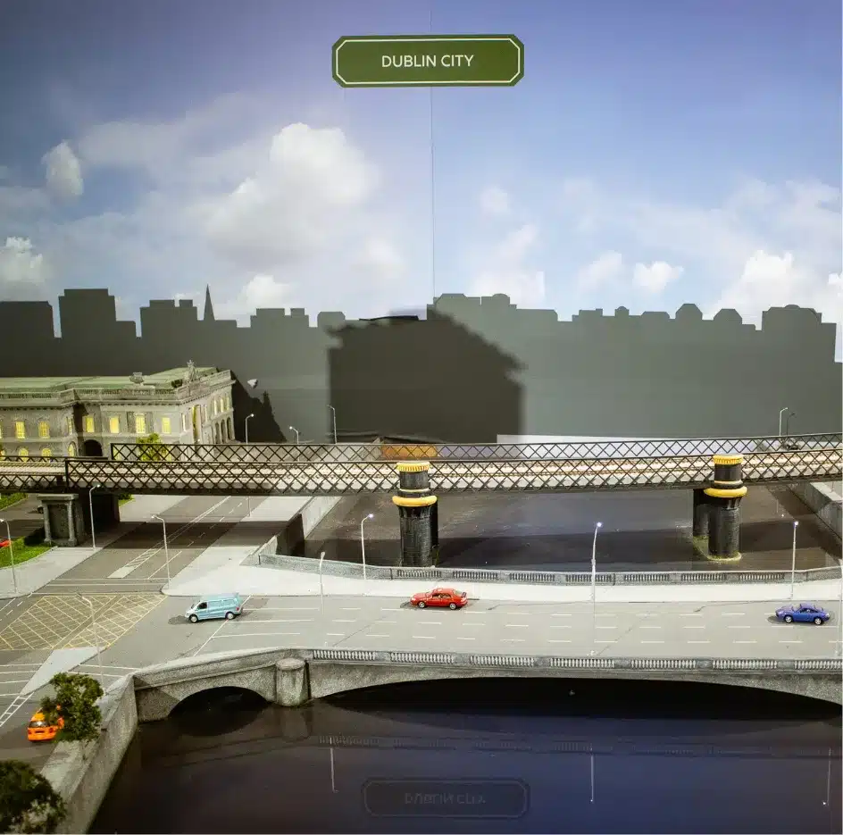 A diorama of Dublin City featuring a bridge over a river with several cars and a building in the background. A sign reads "Dublin City" amidst a clear sky.