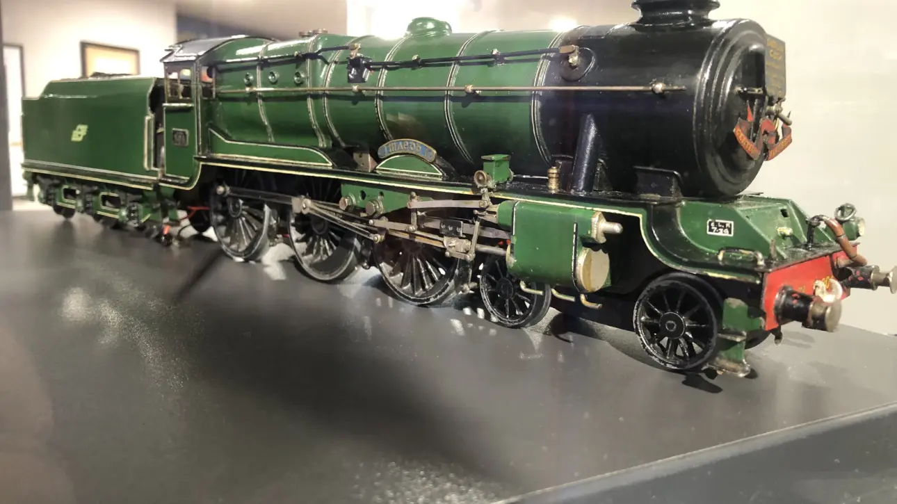 A detailed model of a vintage green steam locomotive with black and gold accents displayed on a reflective surface indoors.