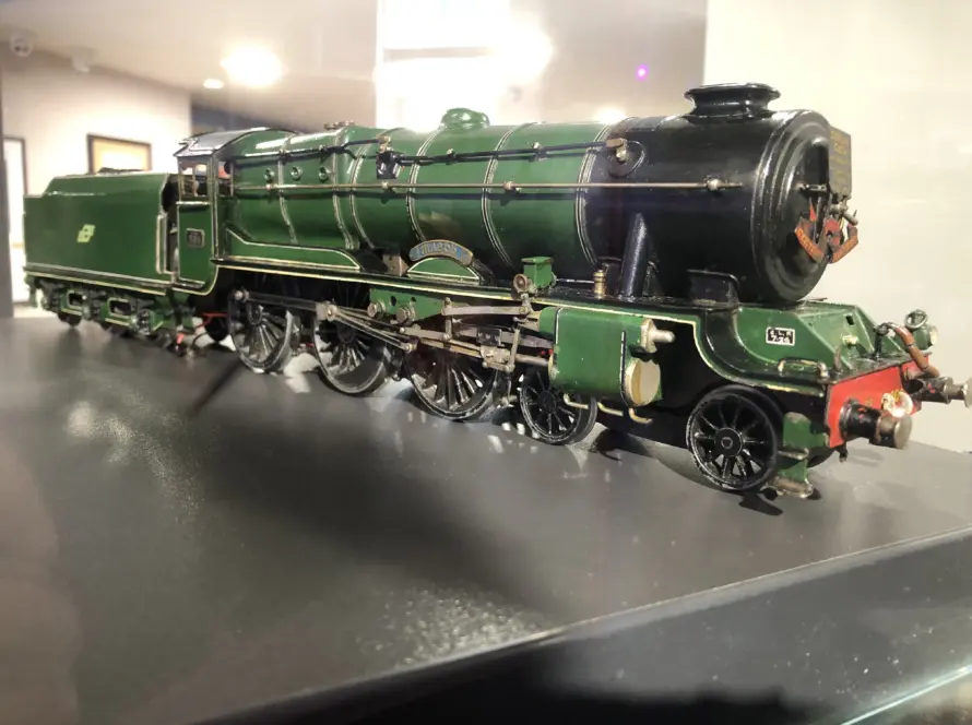 A detailed model of a vintage green steam locomotive with black and gold accents displayed on a reflective surface indoors.