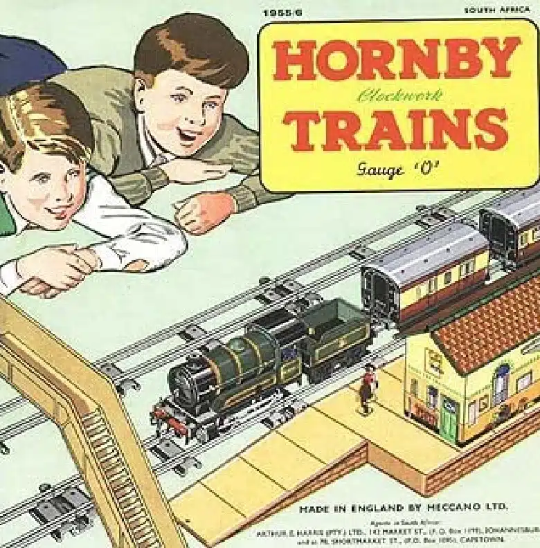 Illustration of two smiling boys lying on the floor playing with a Hornby clockwork train set. The set includes a steam locomotive, passenger cars, and a station building. The text reads “Hornby Trains Gauge 'O'” and “Made in England by Meccano Ltd.”.