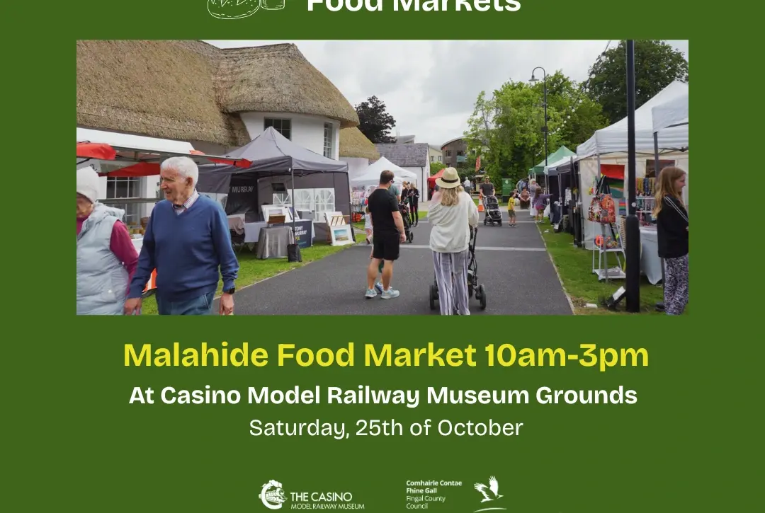 People stroll among stalls at an outdoor food market with tents and a thatched building, surrounded by fresh produce. Join us for Malahide Food Market, part of Fingal Food Markets, on 25th October, 10am-3pm at Casino Model Railway Museum Grounds.