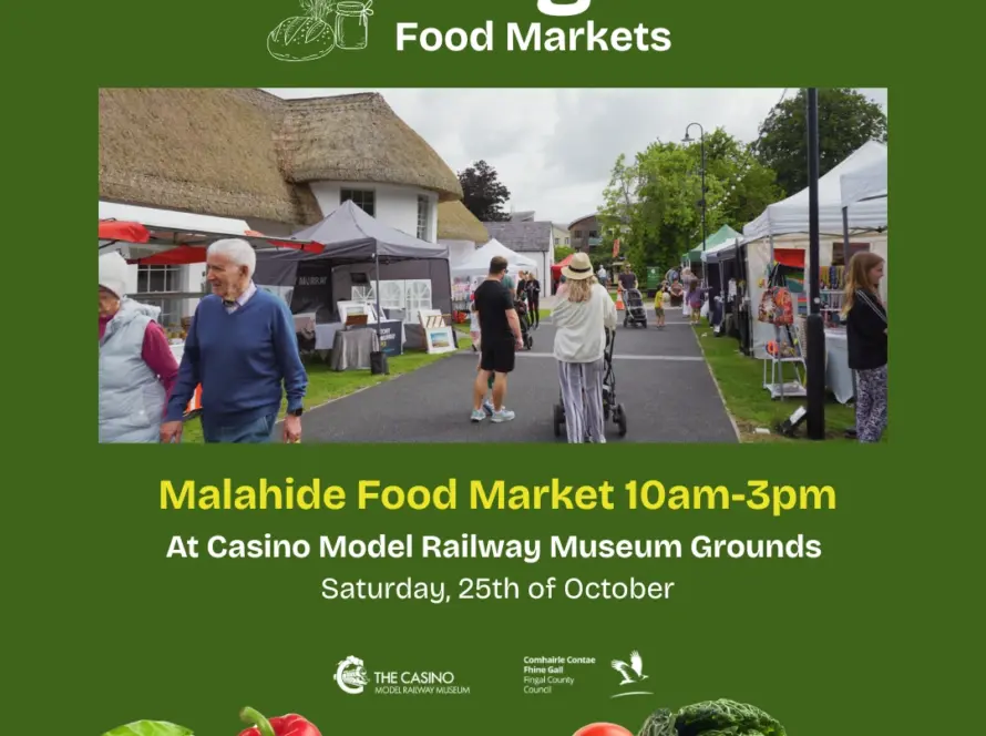 People stroll among stalls at an outdoor food market with tents and a thatched building, surrounded by fresh produce. Join us for Malahide Food Market, part of Fingal Food Markets, on 25th October, 10am-3pm at Casino Model Railway Museum Grounds.