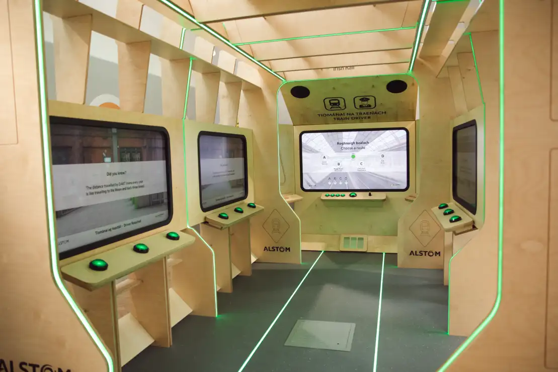 A modern, wood-paneled simulation room with large interactive screens on both sides, green LED lighting accents, and control panels, branded with the Alstom logo—perfect for exploring Irish rail history in Dublin.